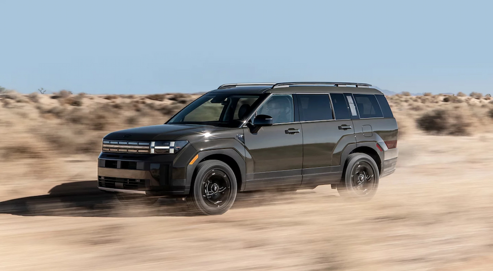A grey 2024 Hyundai Santa Fe XRT driving fast on a dusty road.
