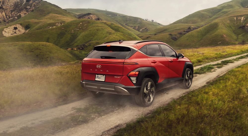 A red 2025 Hyundai Kona Limited driving on a dirt trail through green hills.