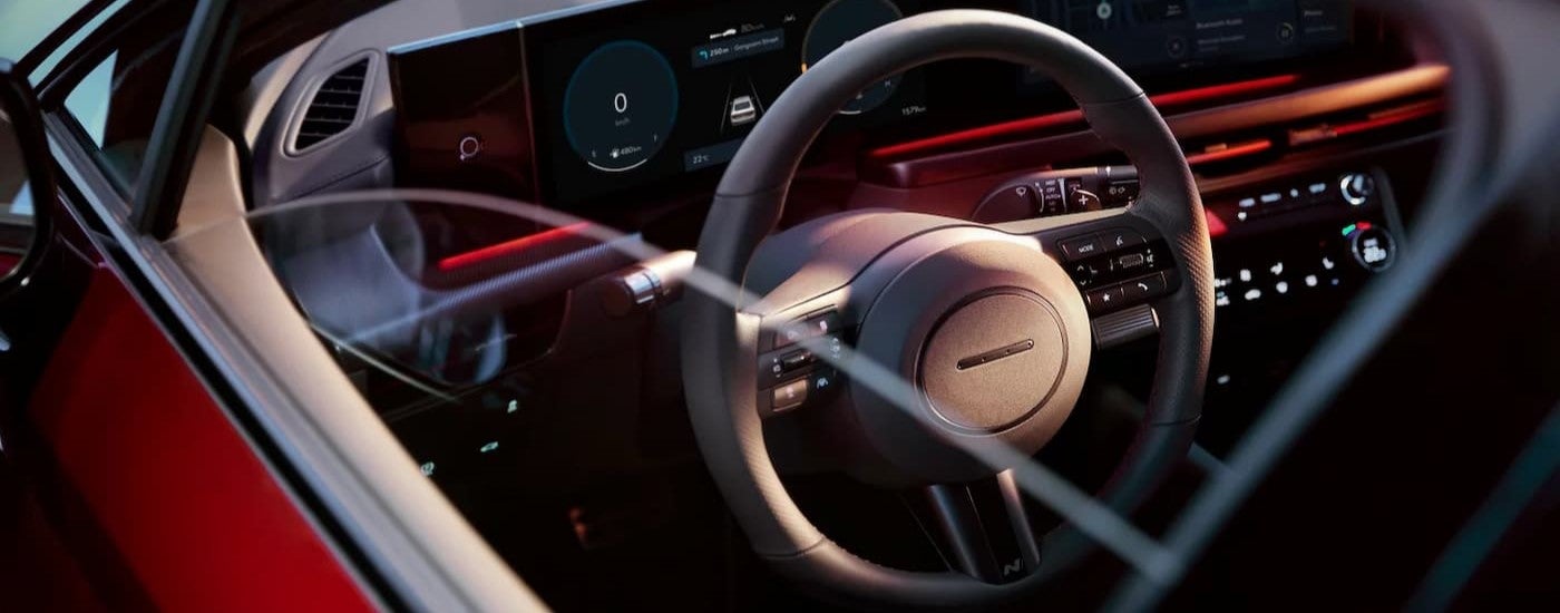 Close-up on the steering wheel and dashboard in the interior of a red 2024 Hyundai Sonata.