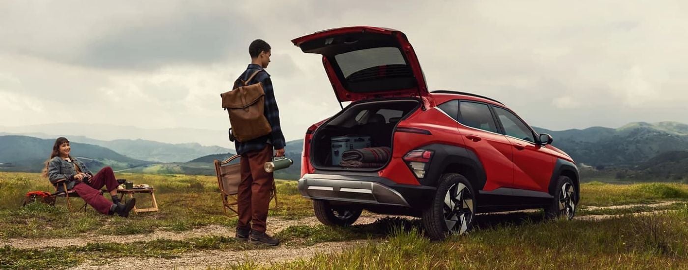 Rear angle view of a man opening the hatchback of a red 2024 Hyundai Kona Limited.