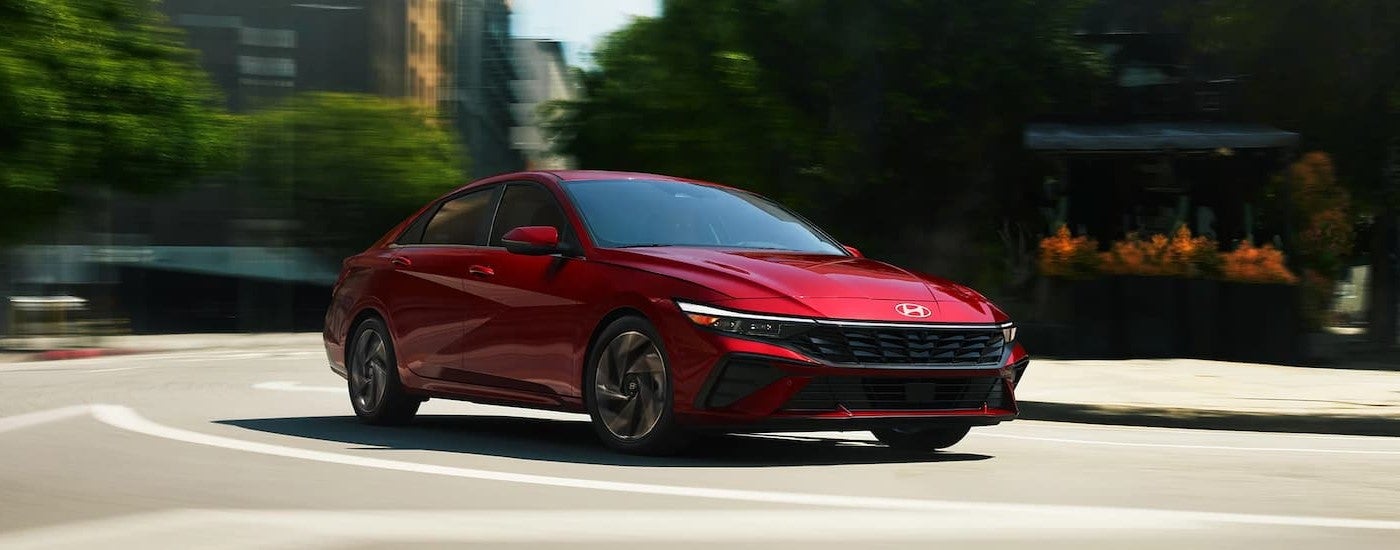A red 2024 Hyundai Elantra driving through a city after visiting a Hyundai dealer near Barrington.