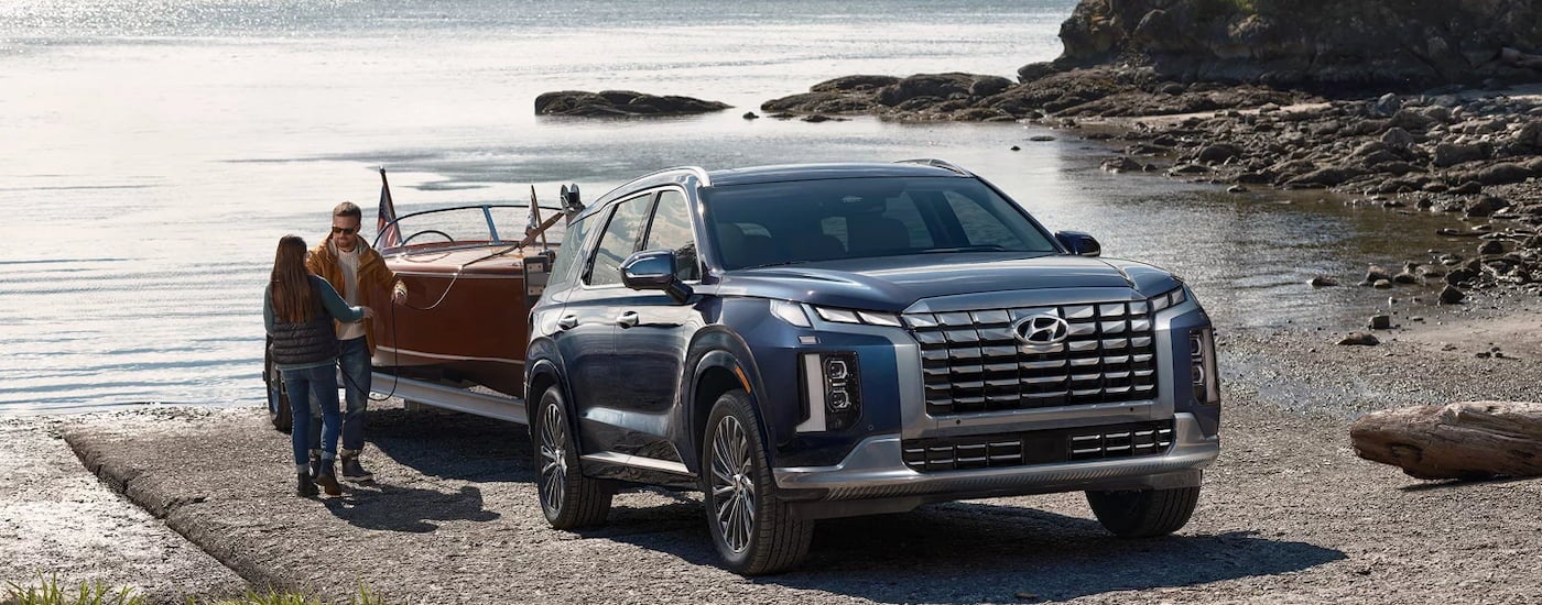 A dark blue 2024 Hyundai Palisade towing a boat out of a lake.