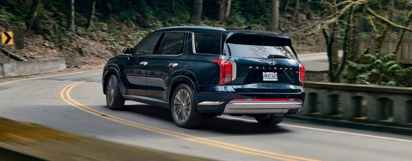 Rear view of a dark blue 2024 Hyundai Palisade driving around a bend.