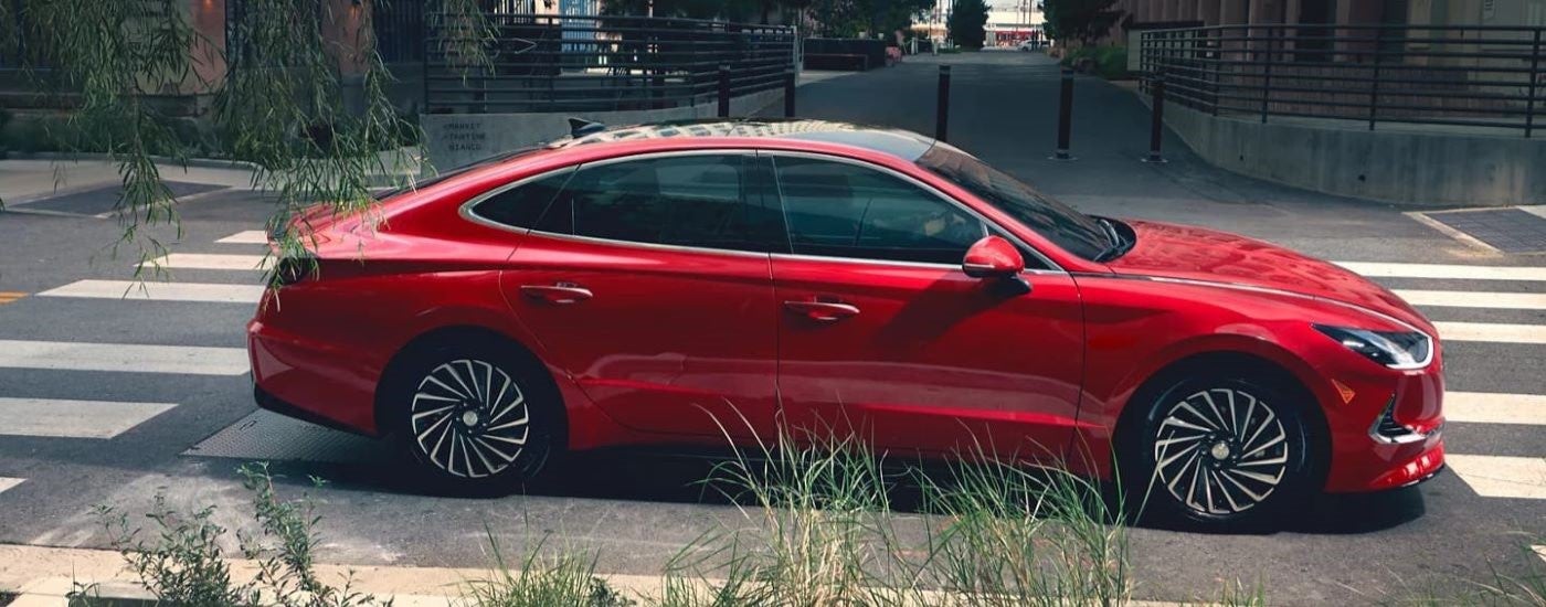 A red 2021 Hyundai Sonata Hybrid driving in a city after visiting a used Hyundai dealership.